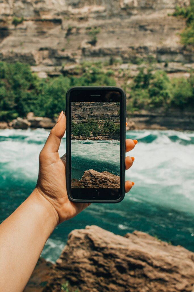 Hand holding smartphone capturing the stunning view of Niagara Falls rapids.