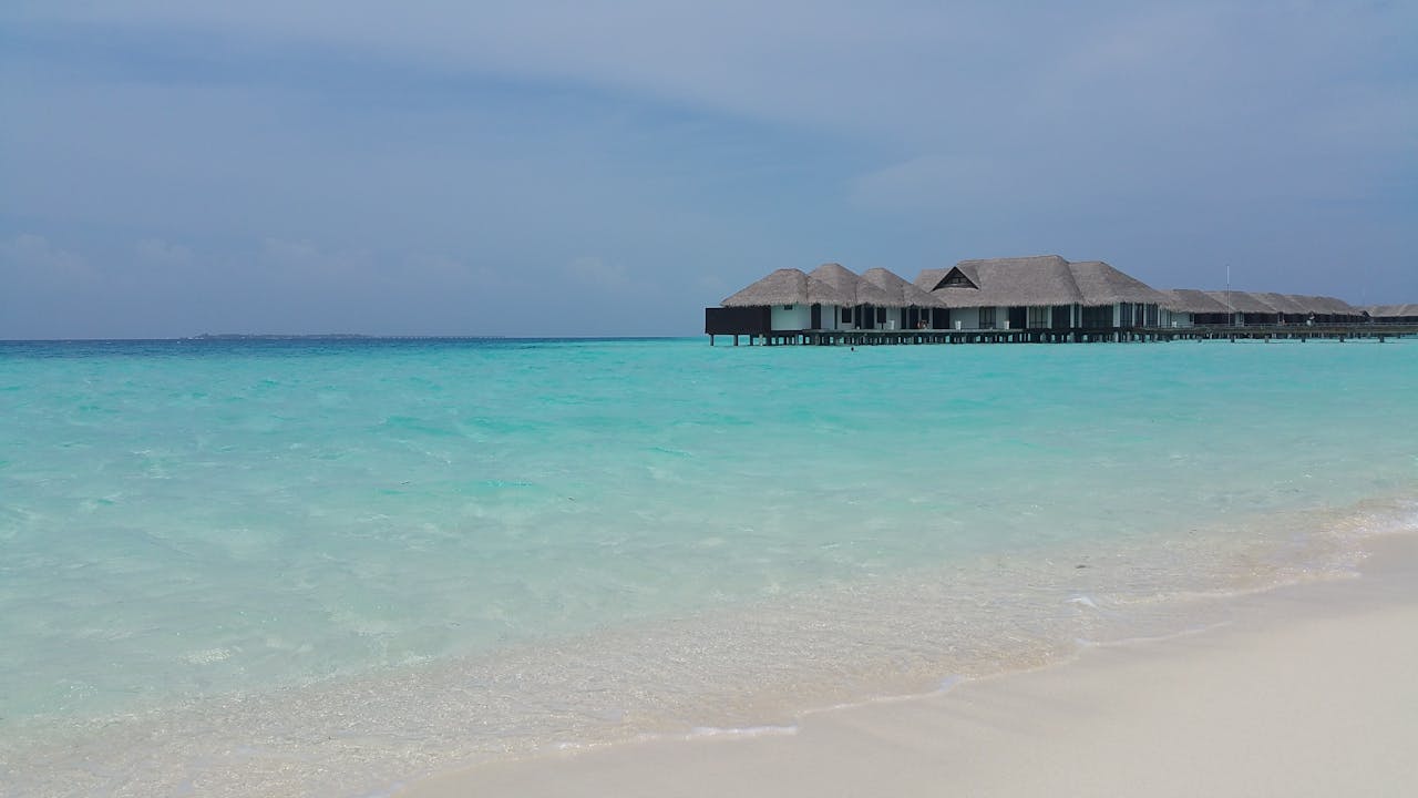 Serene tropical beach scene with turquoise water and thatched roof bungalows in Maldives.